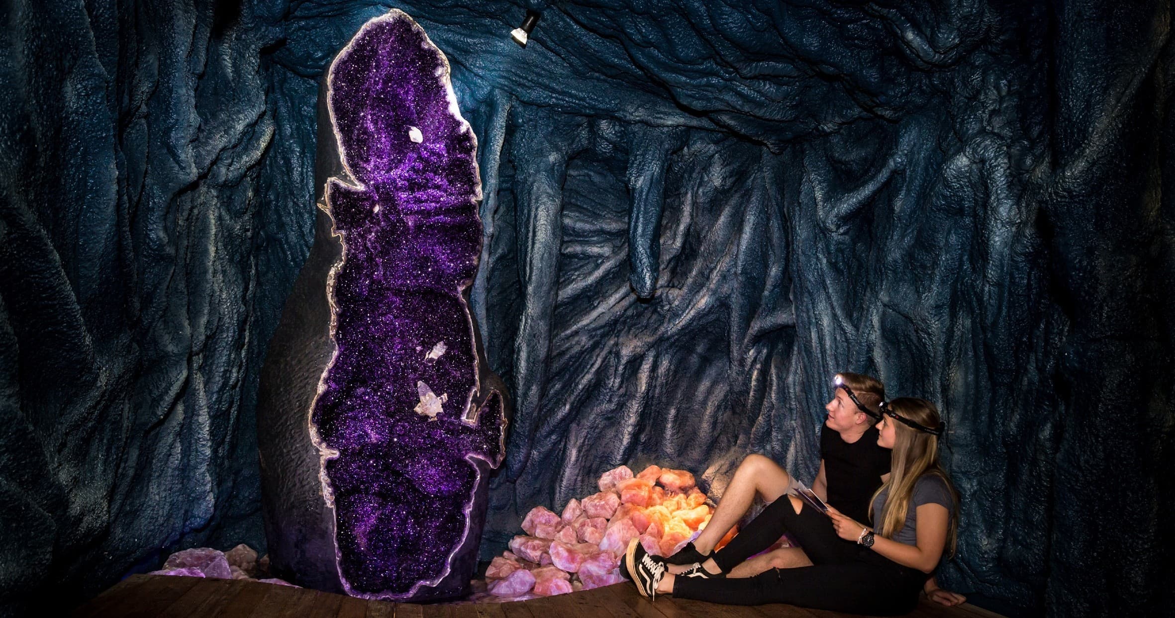 Visitor viewing giant amethyst geode inside dark cave exhibit
