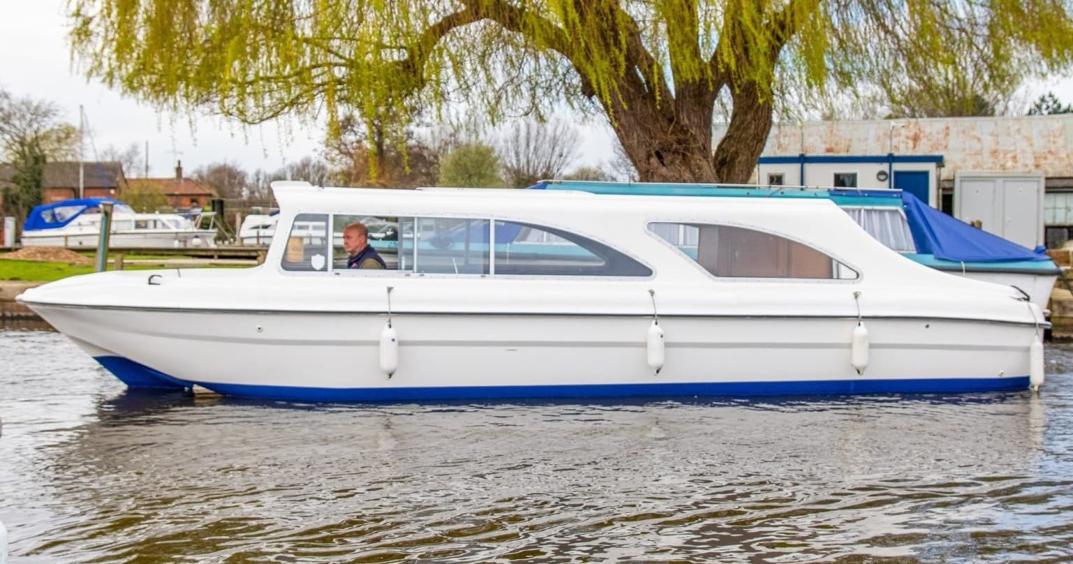 Long leisure launch cruising past willow trees on riverbank