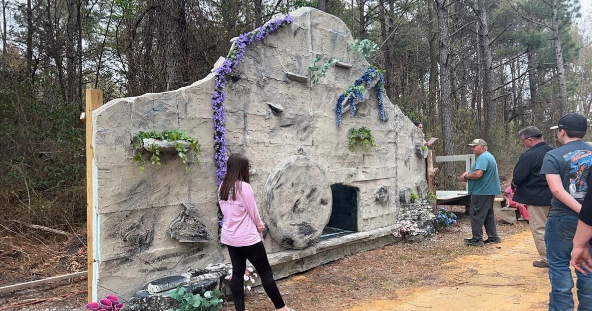 Visitors examining artificial rock grotto in wooded outdoor display