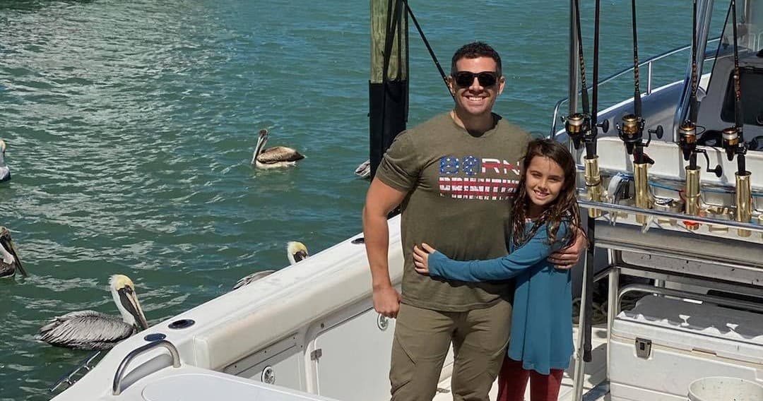 Father and daughter smiling on docked boat with pelicans nearby