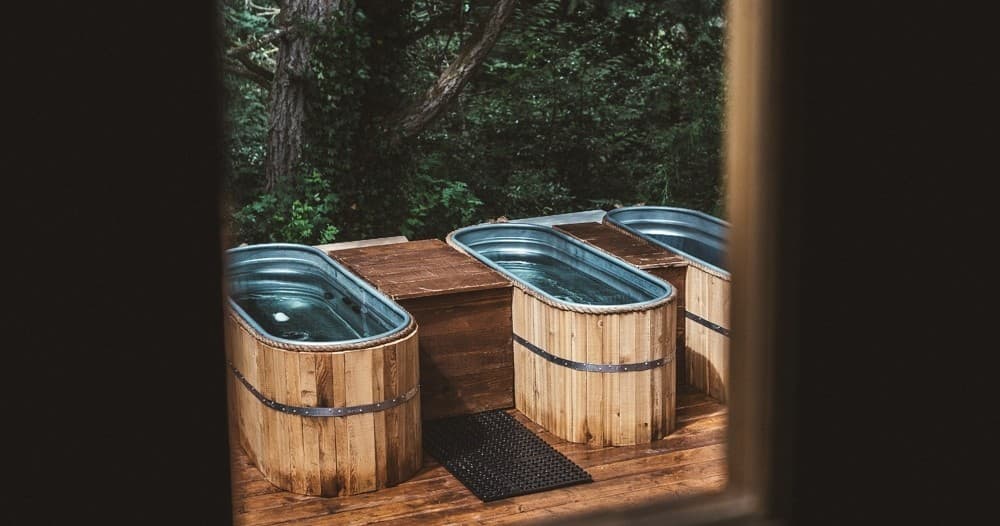 Three wooden outdoor hot tubs on deck framed by forest