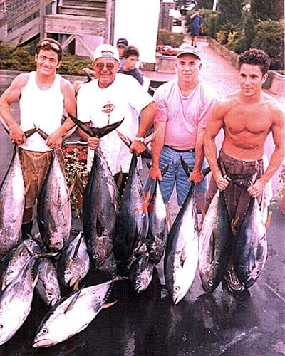 Group of anglers displaying tuna catch on marina pier after charter trip