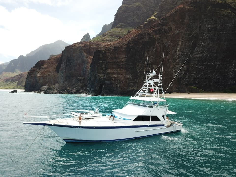 White sportfishing yacht near rugged sea cliffs and turquoise shore