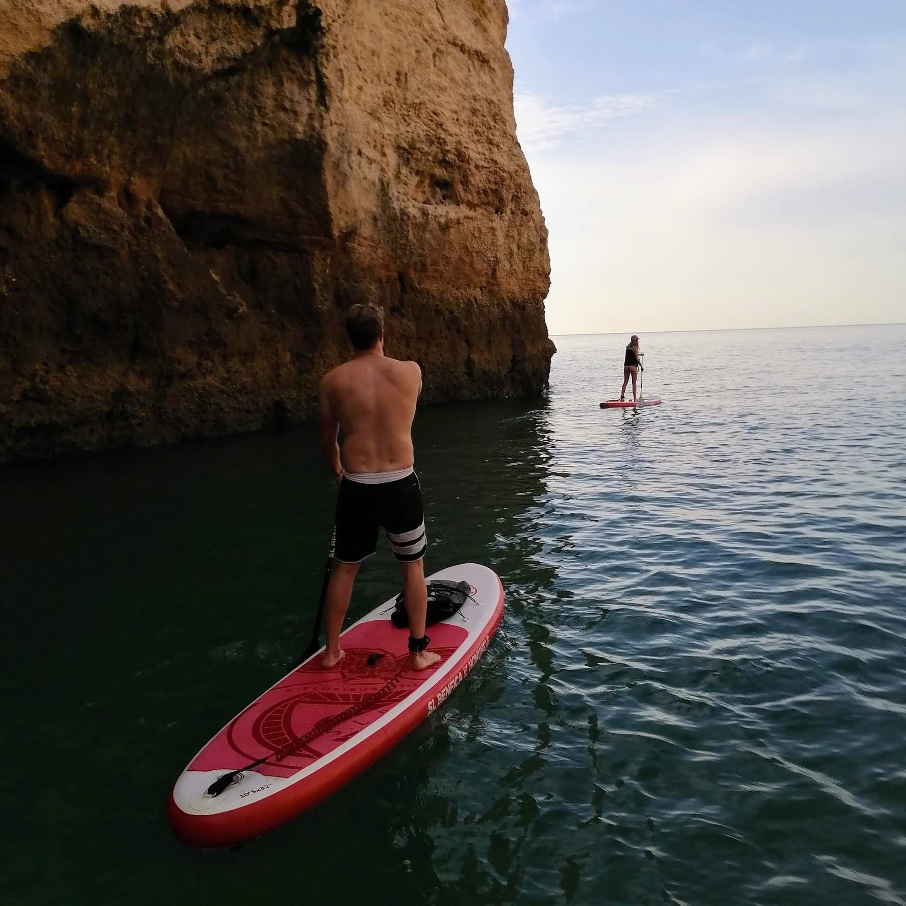 Paddleboarder cruising near sea cliffs at golden-hour coastline