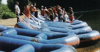 Group preparing inflatable rafts at riverbank for guided whitewater trips