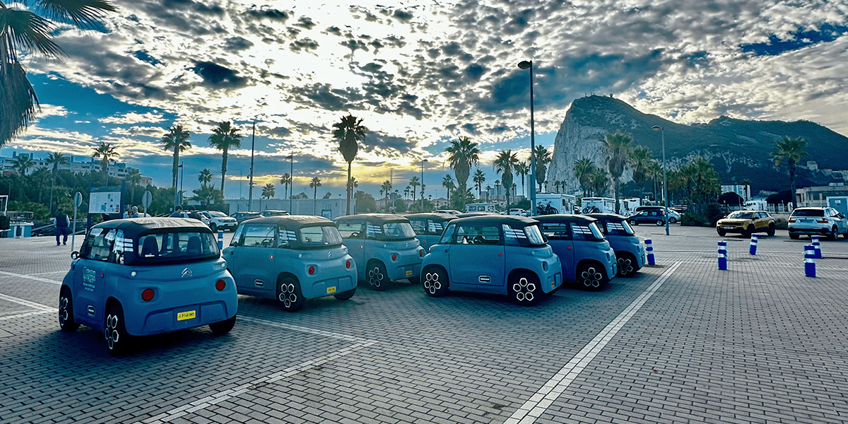 Electric microcars parked in coastal lot near palm-lined promenade