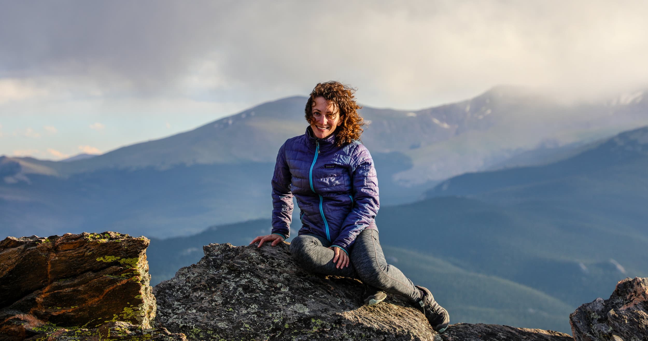 Hiker resting on rocky outcrop overlooking valley and peaks