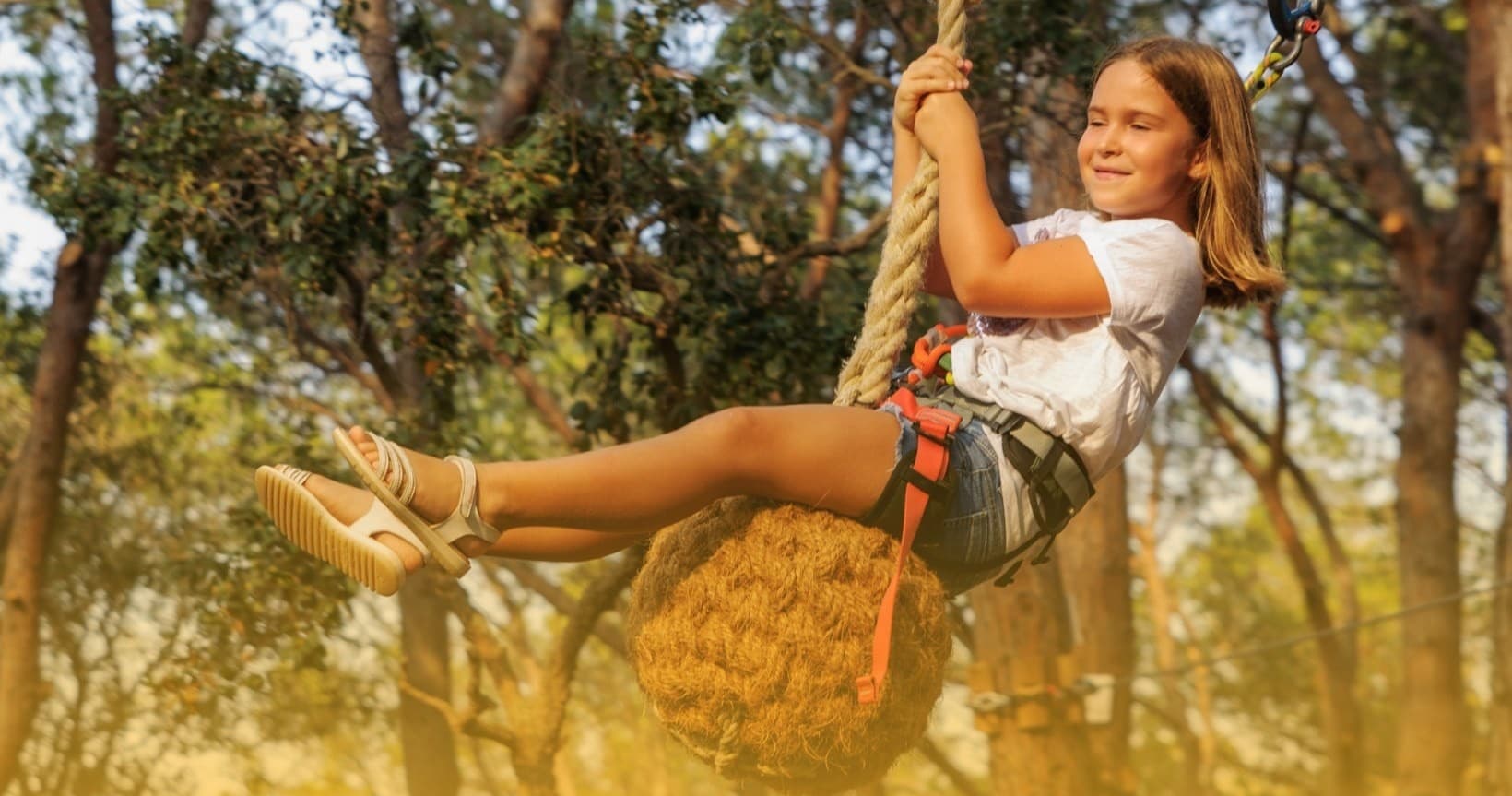Child on rope swing through wooded park, joyful outdoor play