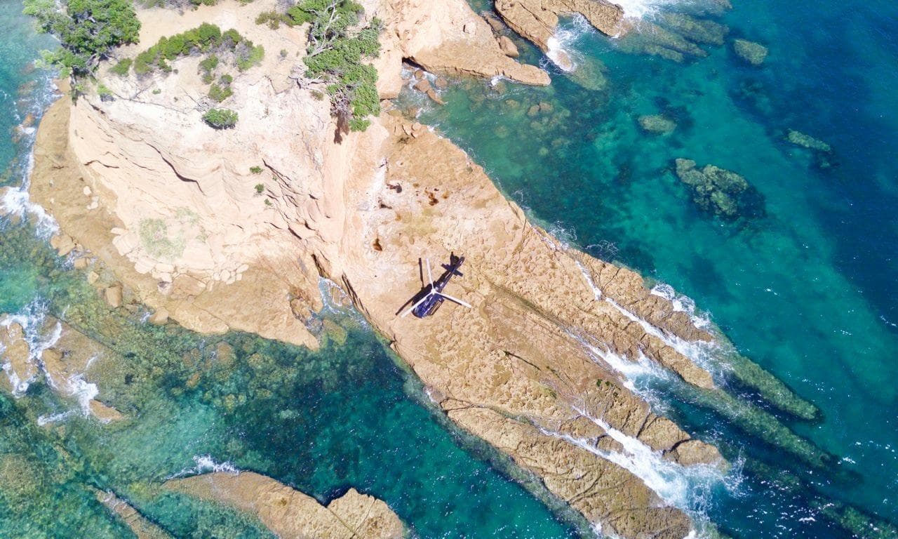 Birds-eye coastal panorama with helicopter on rocky cliffs