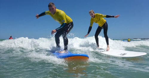 Two surfers balancing on small waves under clear blue sky