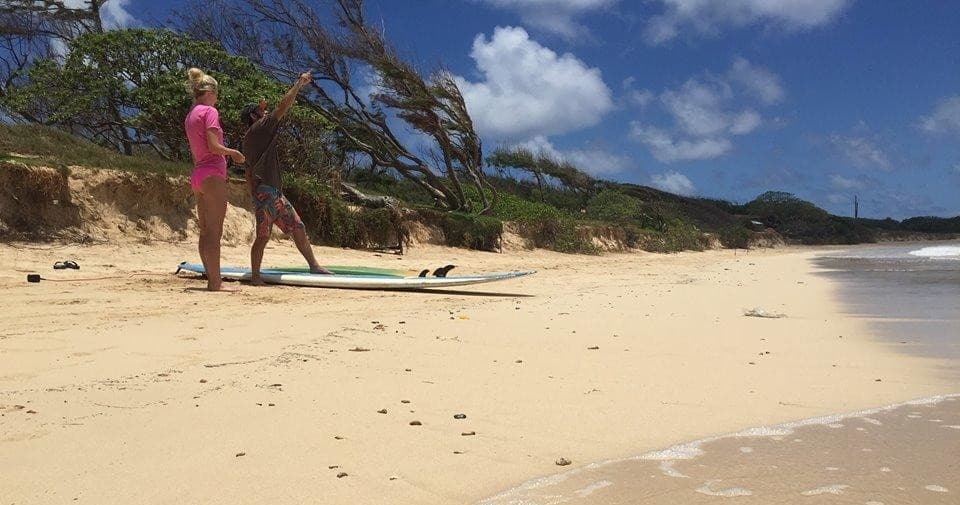 Instructor guiding beginner surfer on quiet sandy beach with trees