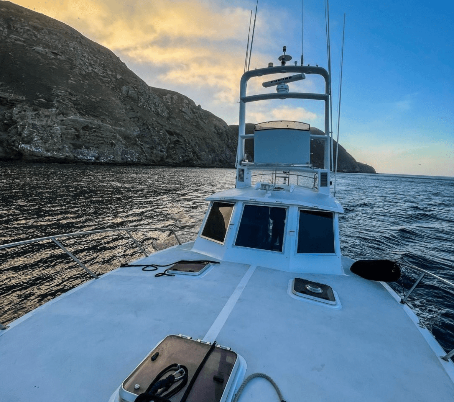Fishing charter bow approaching rocky coastline at sunset