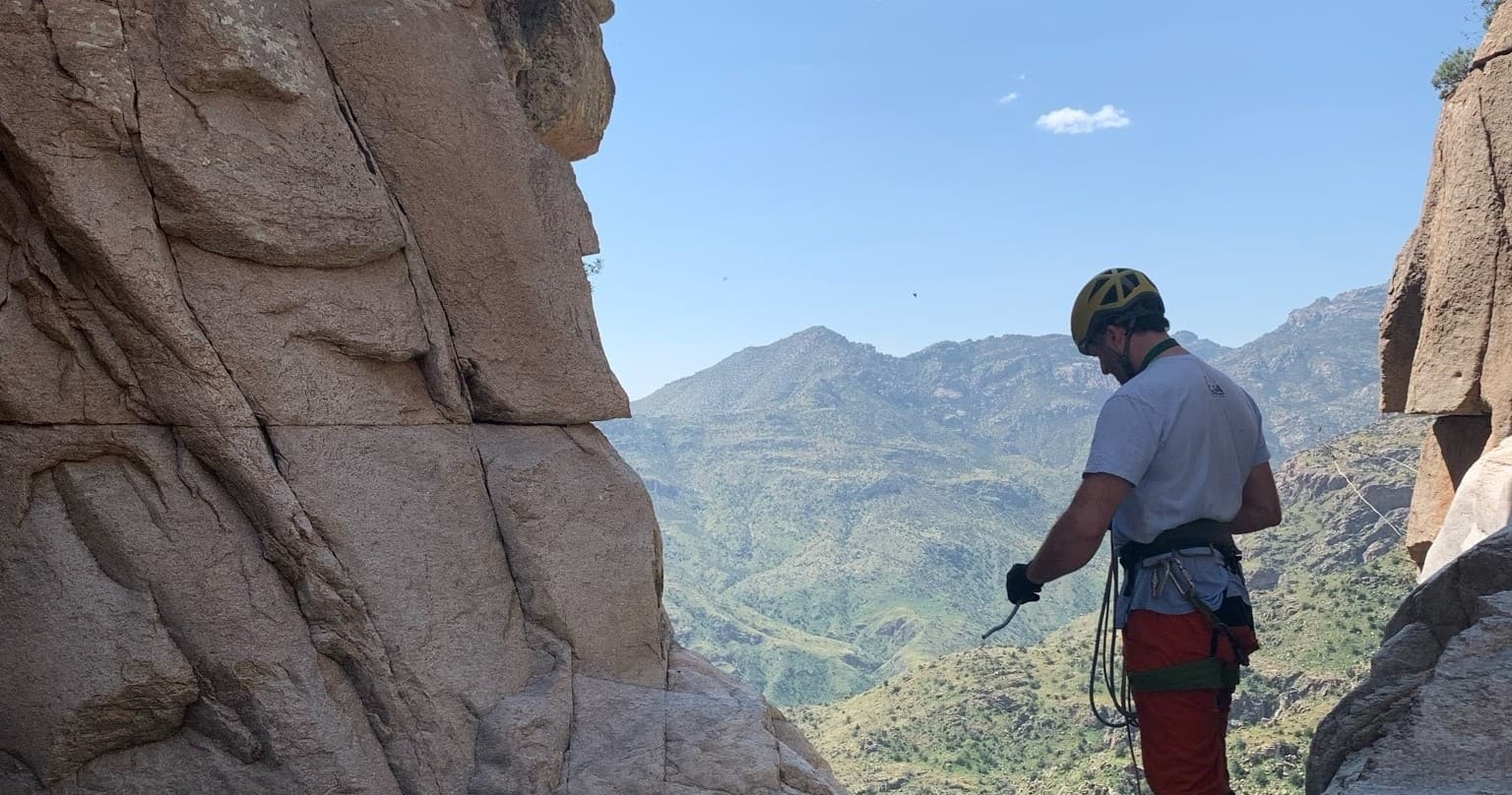 Rock climber silhouetted in rock arch framing valley vista
