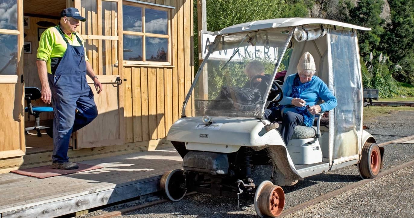 Small rail cart parked at rural station platform, staff assisting