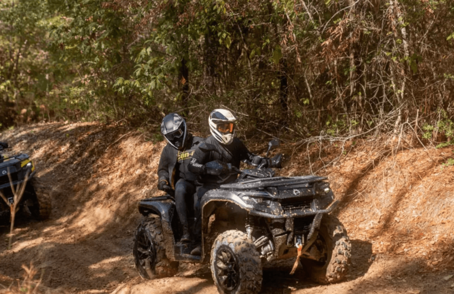 Two riders on an ATV navigating a shaded forest trail