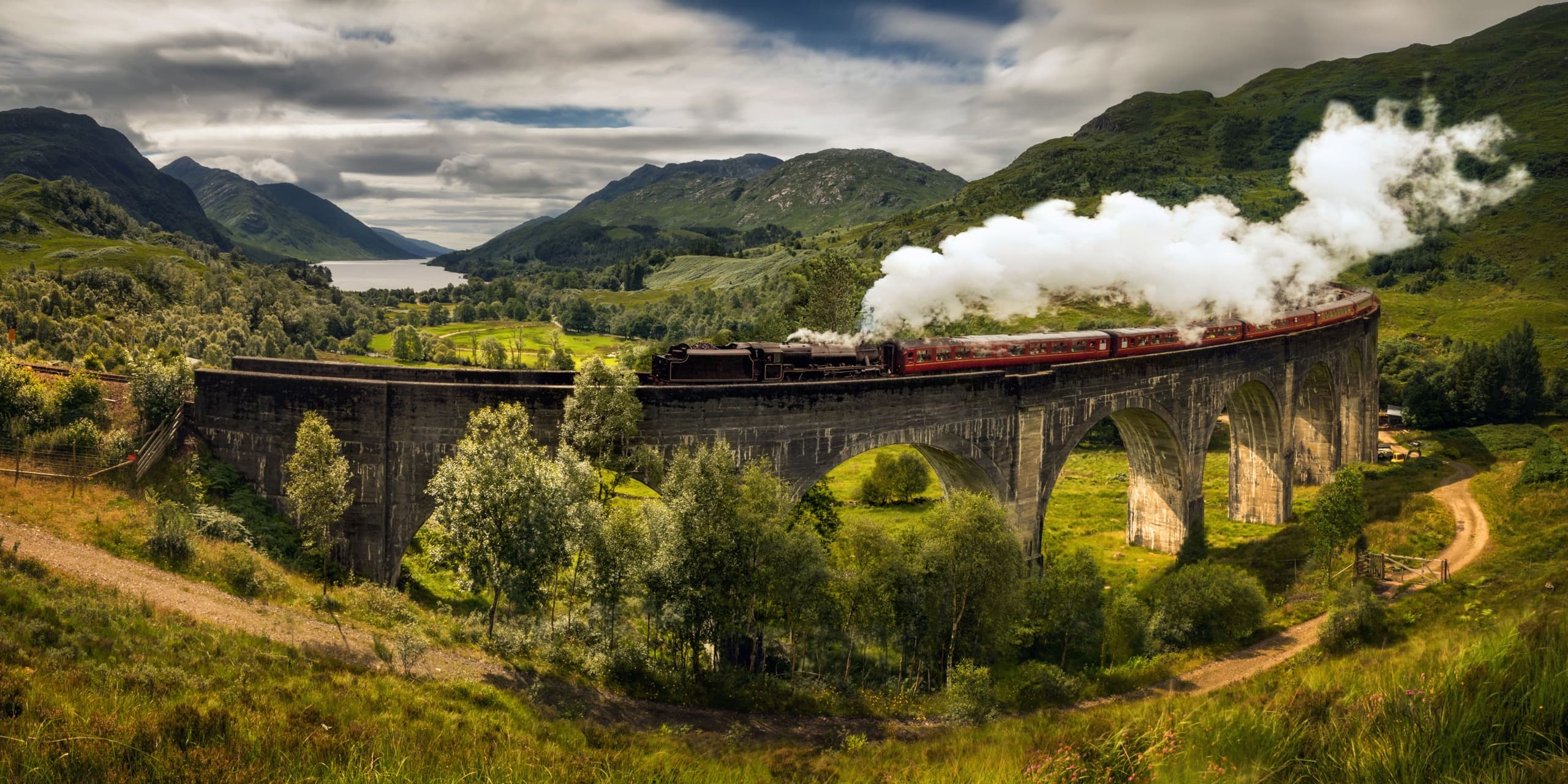 Vintage steam train traversing stone viaduct in Scottish glen