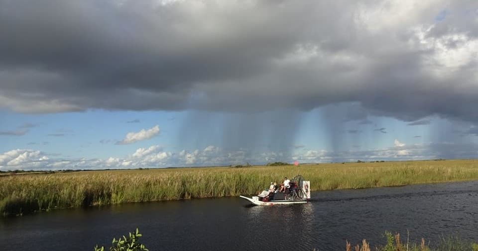 Airboat skimming Everglades marsh under dramatic storm clouds