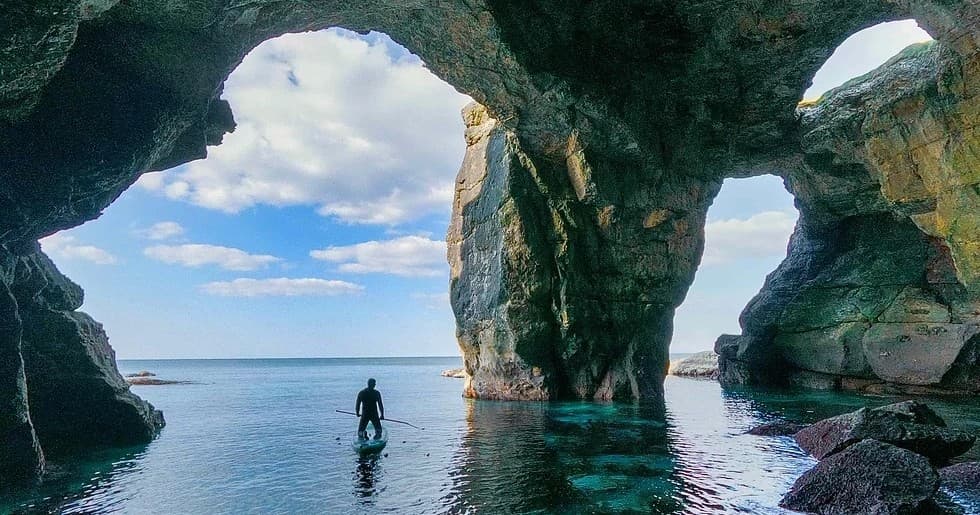 Person wading under coastal sea arches with blue sky view