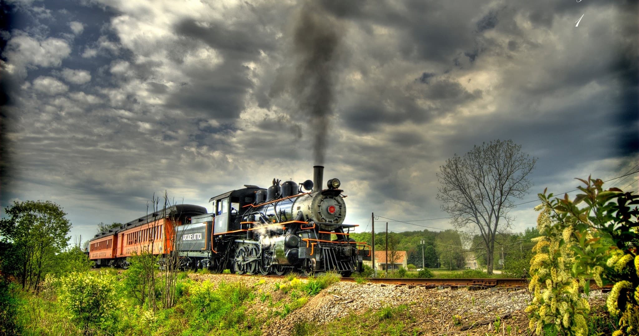 Steam train crossing countryside under dramatic cloudy sky