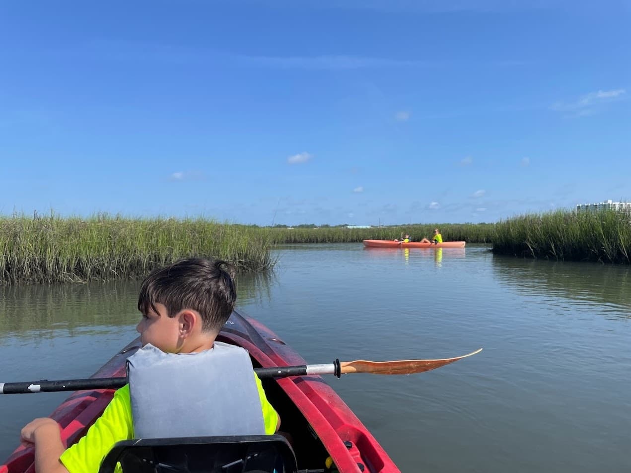 Child kayaking through marsh channel on sunny summer day