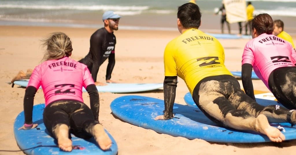 Surf students lying on boards on sandy beach with instructor