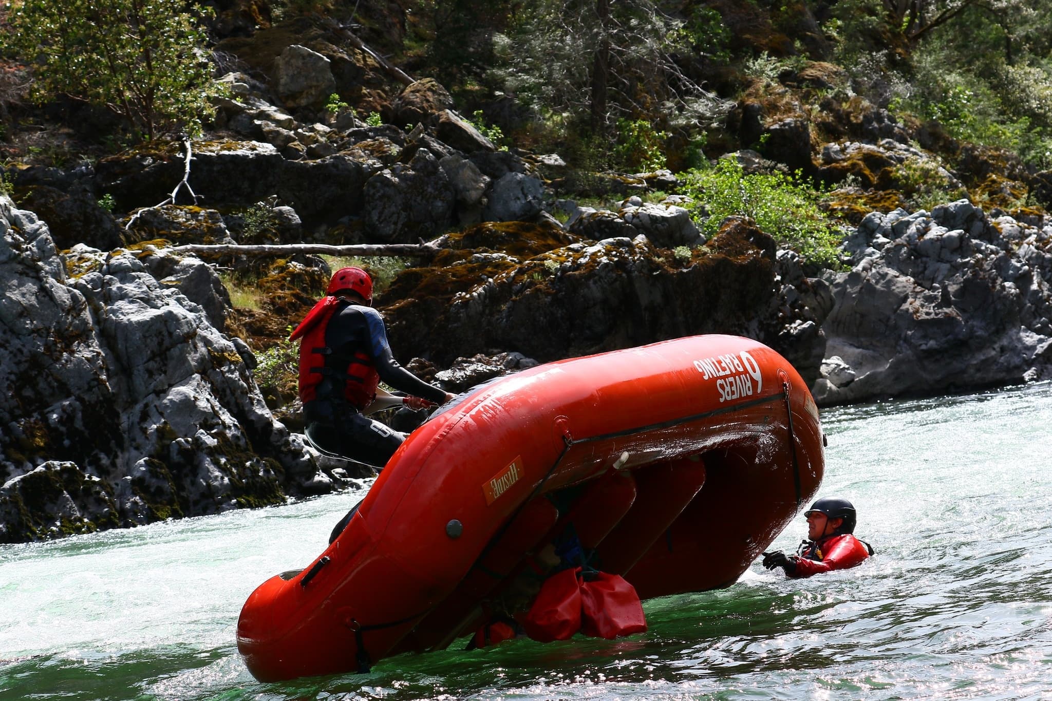 Raft flipped in rocky whitewater with paddlers navigating rescue