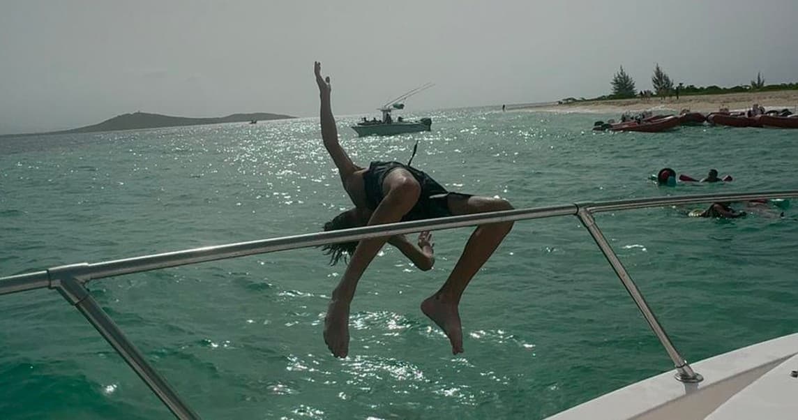 Person diving off charter boat into clear tropical sea near shore
