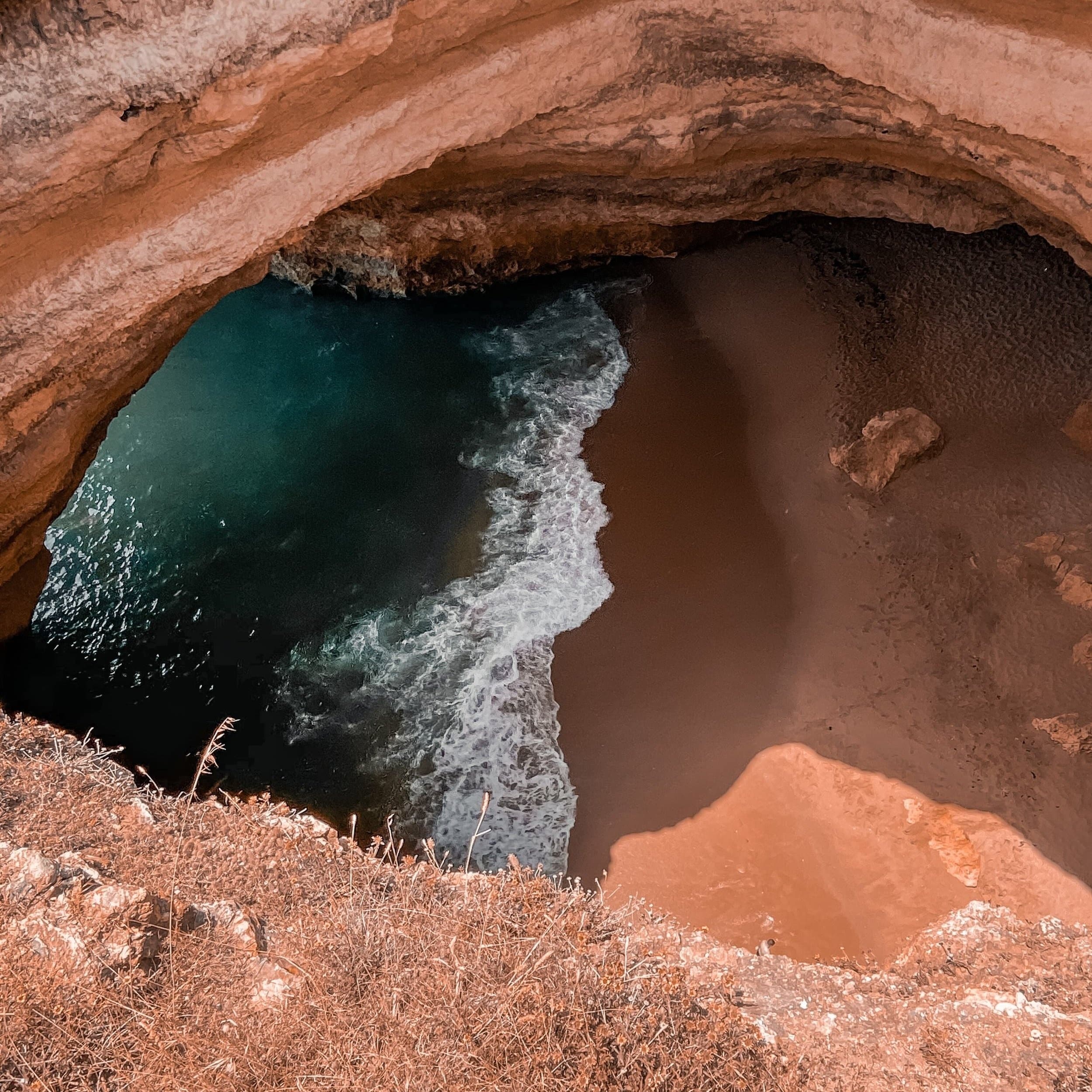 Aerial view of sea cave opening to beach, coastal rock formations and waves