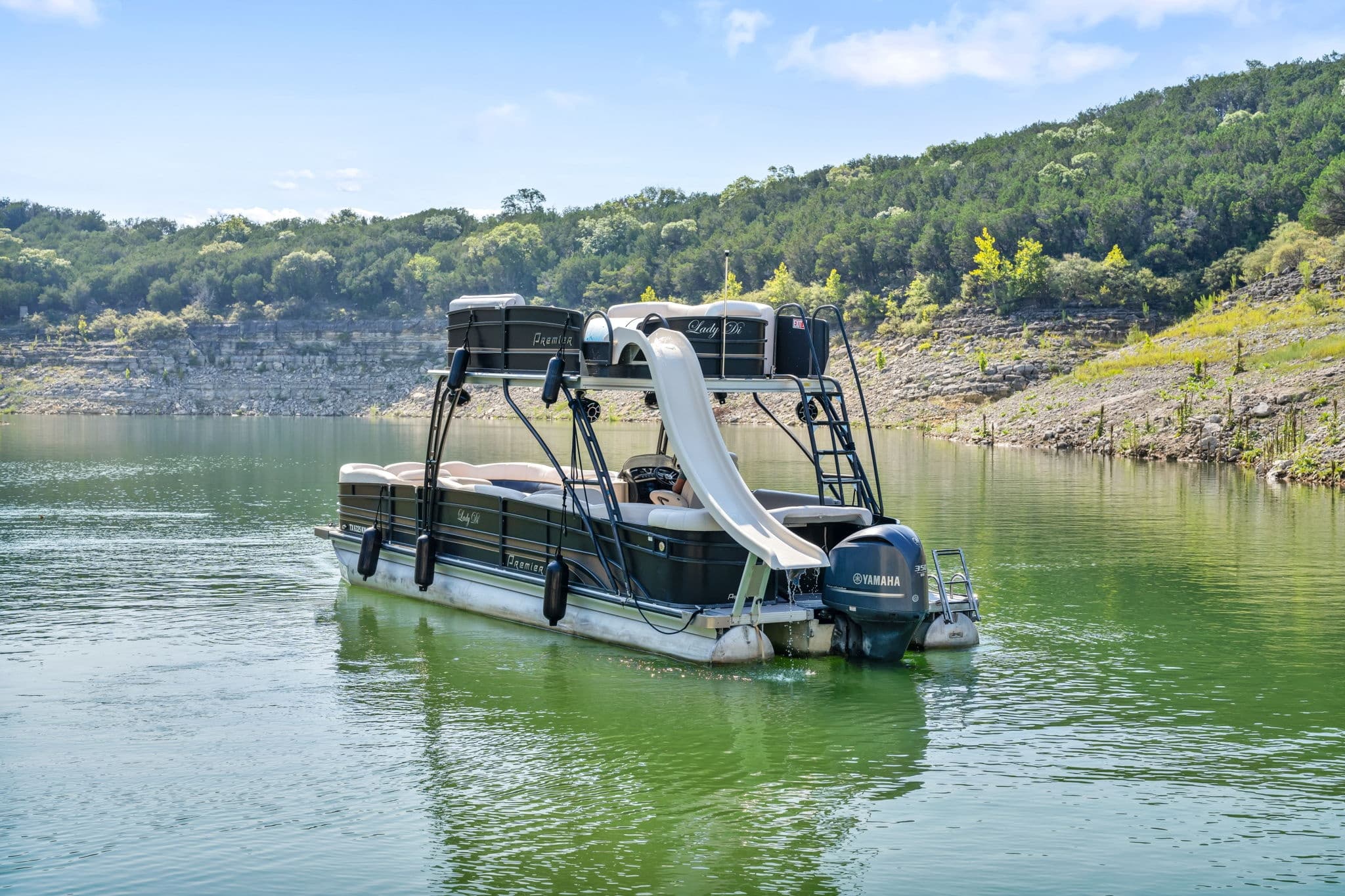 Anchored party pontoon with slide on calm green lake, hills