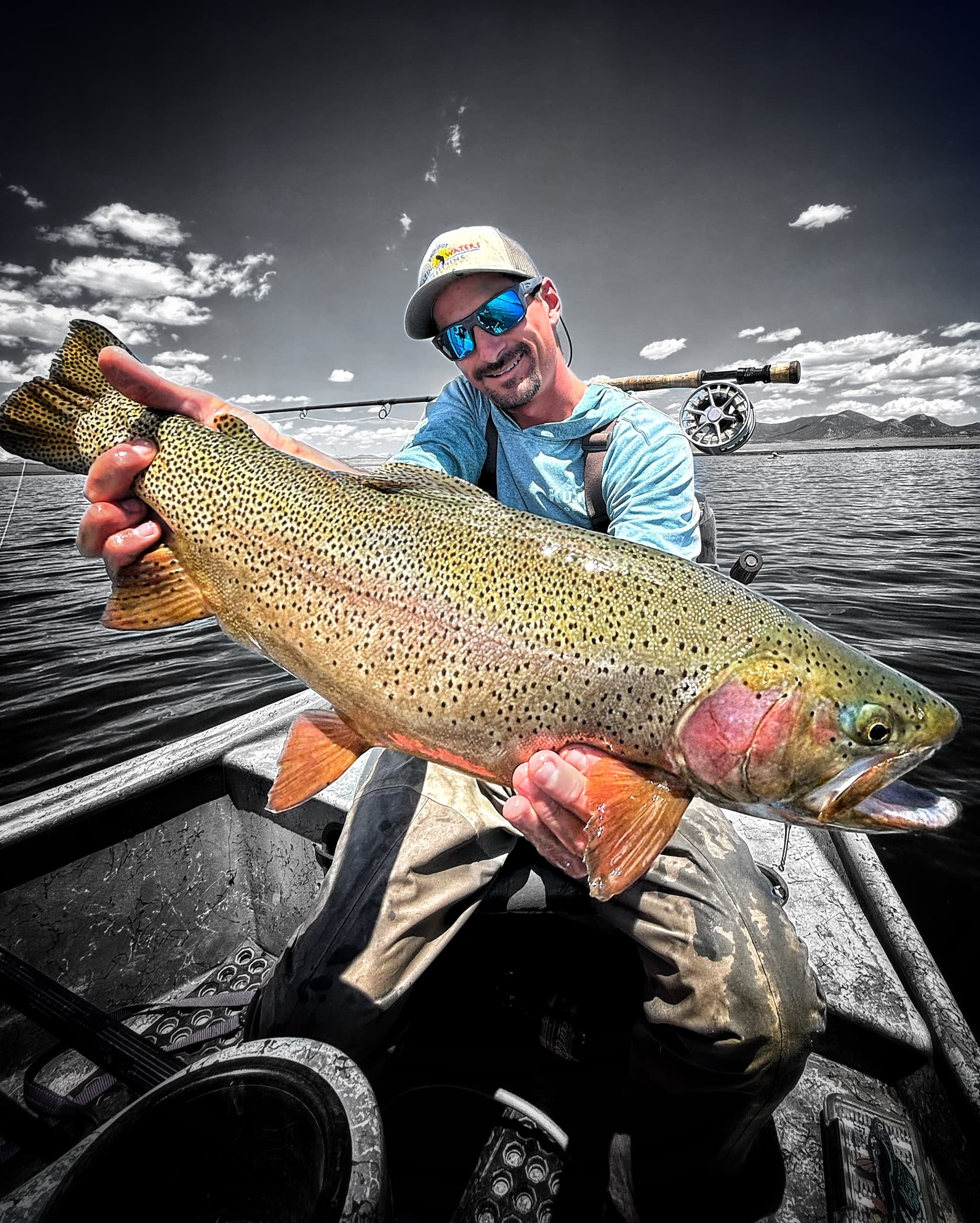 Angler holding giant rainbow trout on boat under dramatic sky