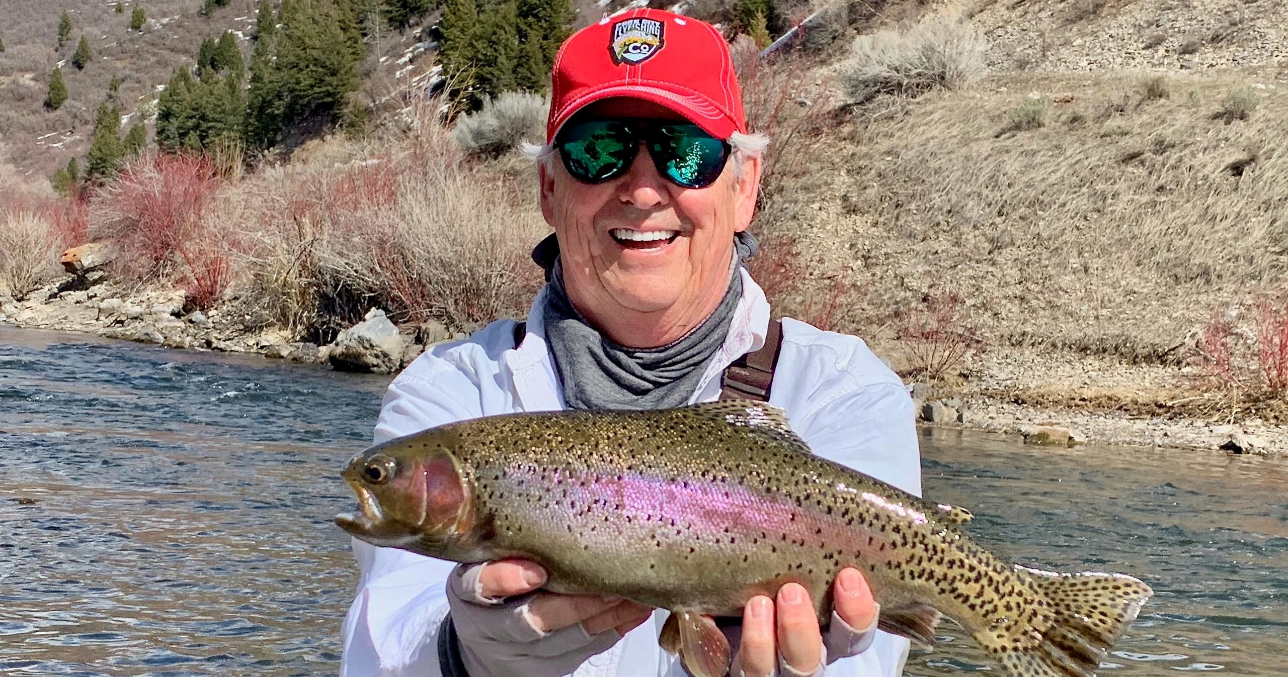 Smiling angler showing rainbow trout with mountain hillside