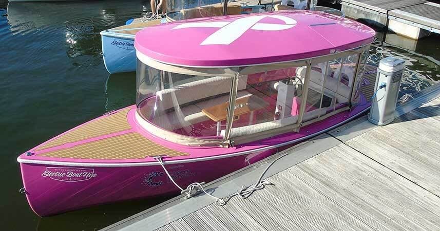 Pink electric tour boat moored at dock in urban marina