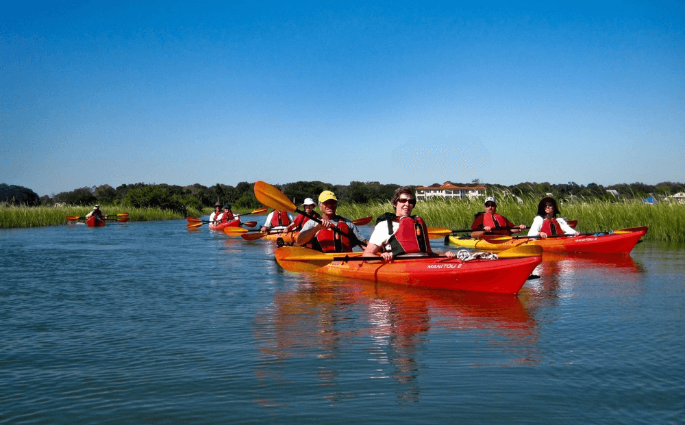 Group kayaking tour on calm marsh waterways under blue sky