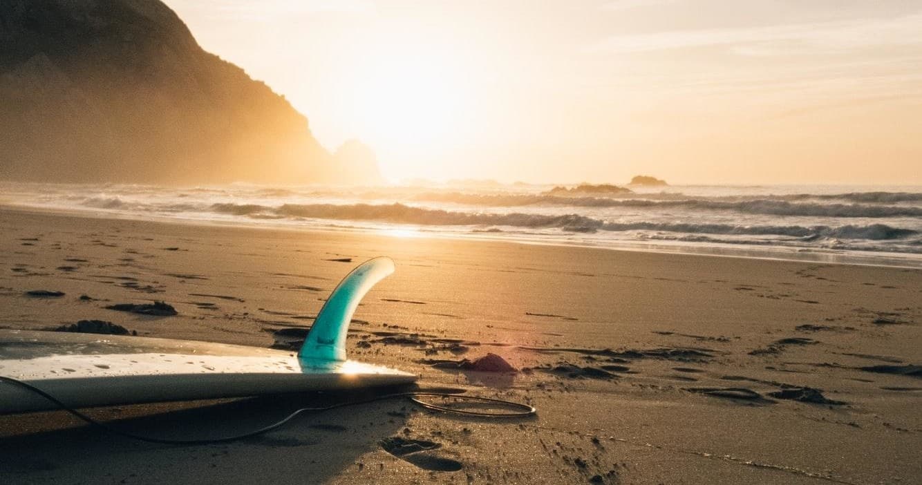 Sunset surfboard fin resting on sandy beach at golden hour