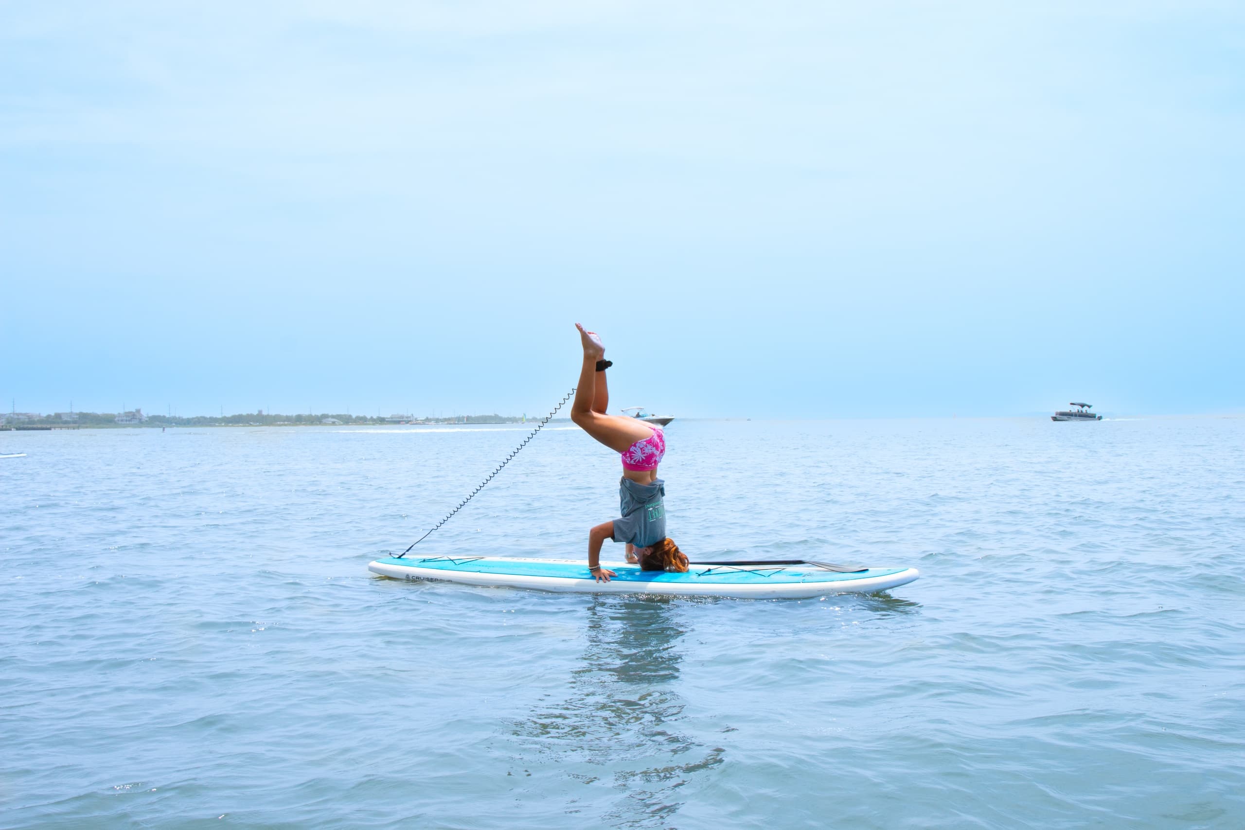 Stand-up paddleboarder performing handstand on calm bay