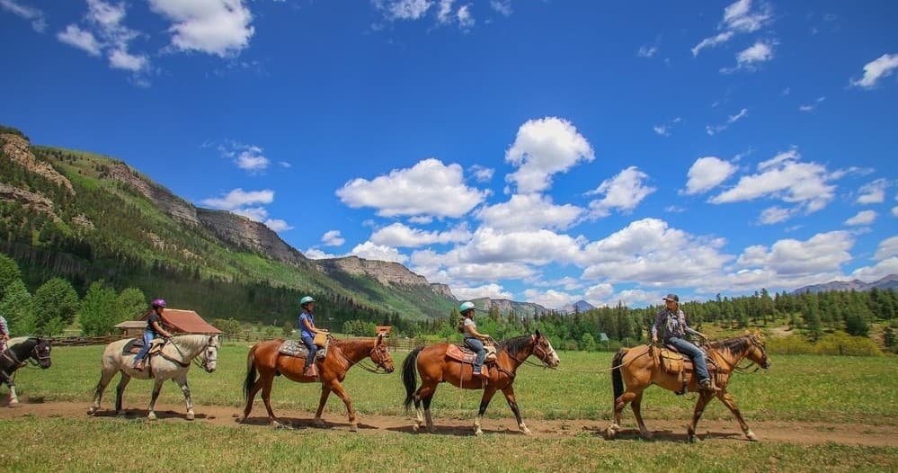 Group trail riders crossing mountain valley under blue sky