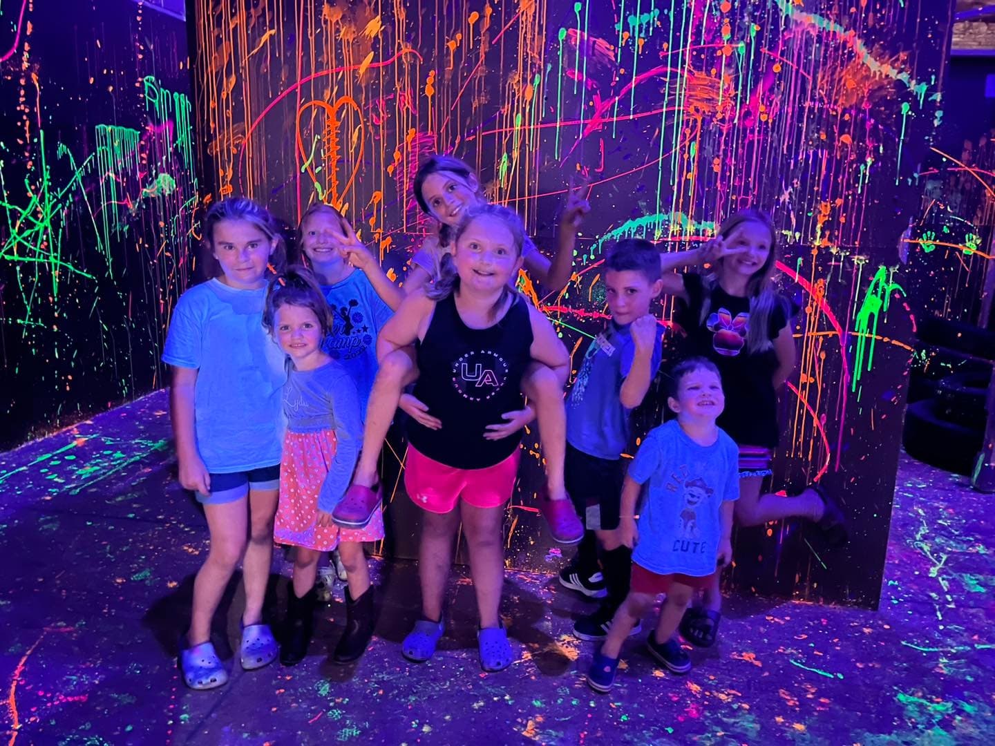Kids enjoying neon splatter paint activity in blacklight room