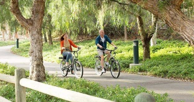 Two cyclists enjoying shaded park electric bike ride under trees