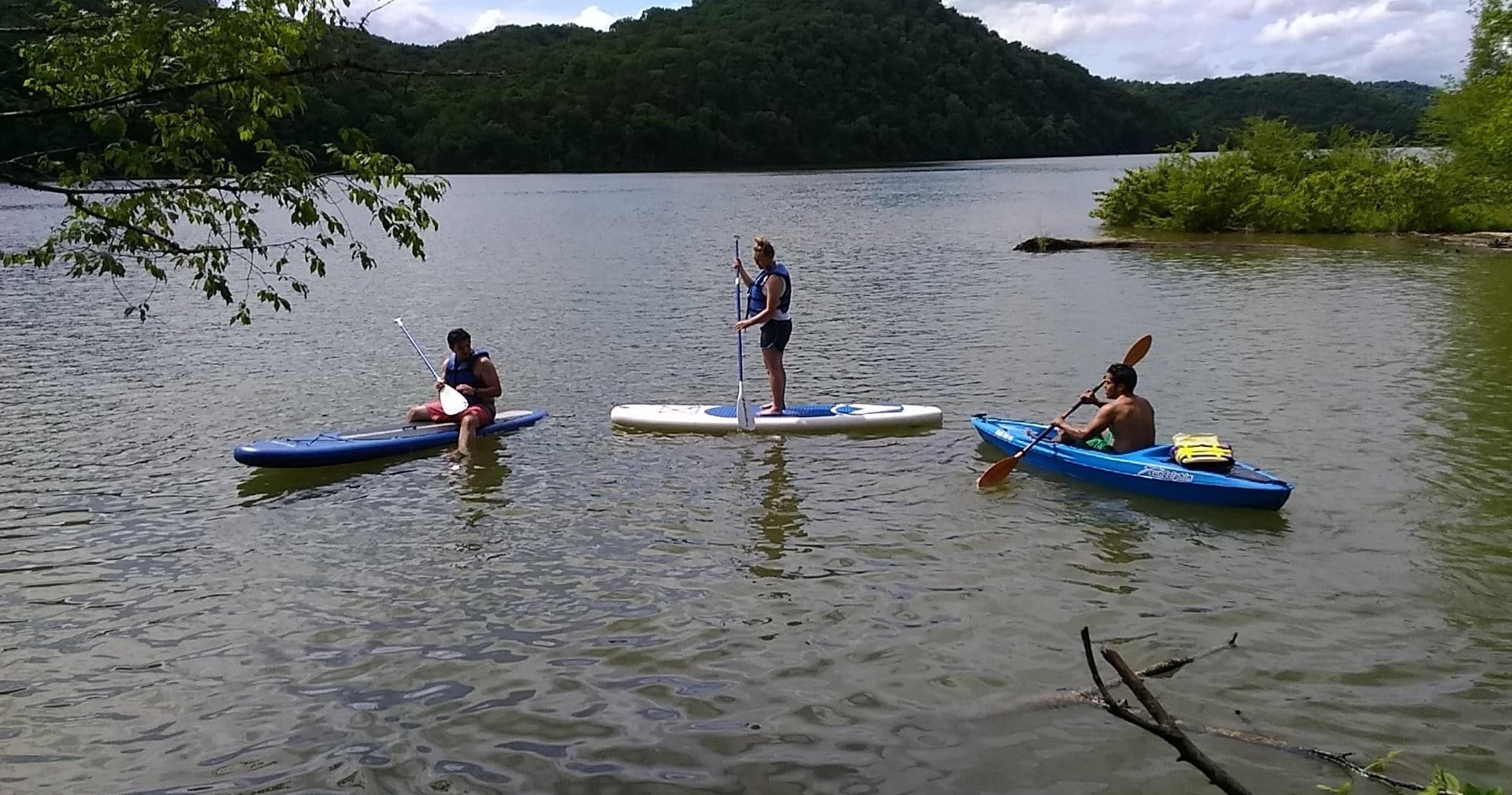 Standup paddleboarders and kayakers paddling on forested lake