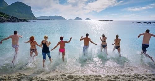 Group running into surf on tropical beach, energetic seaside fun