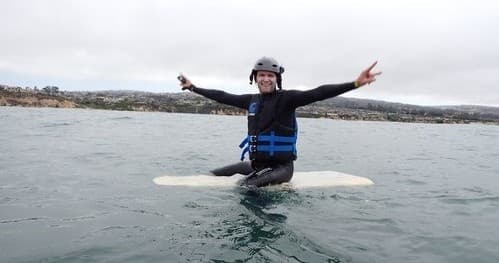 Surfer kneeling on board wearing helmet and life vest in bay