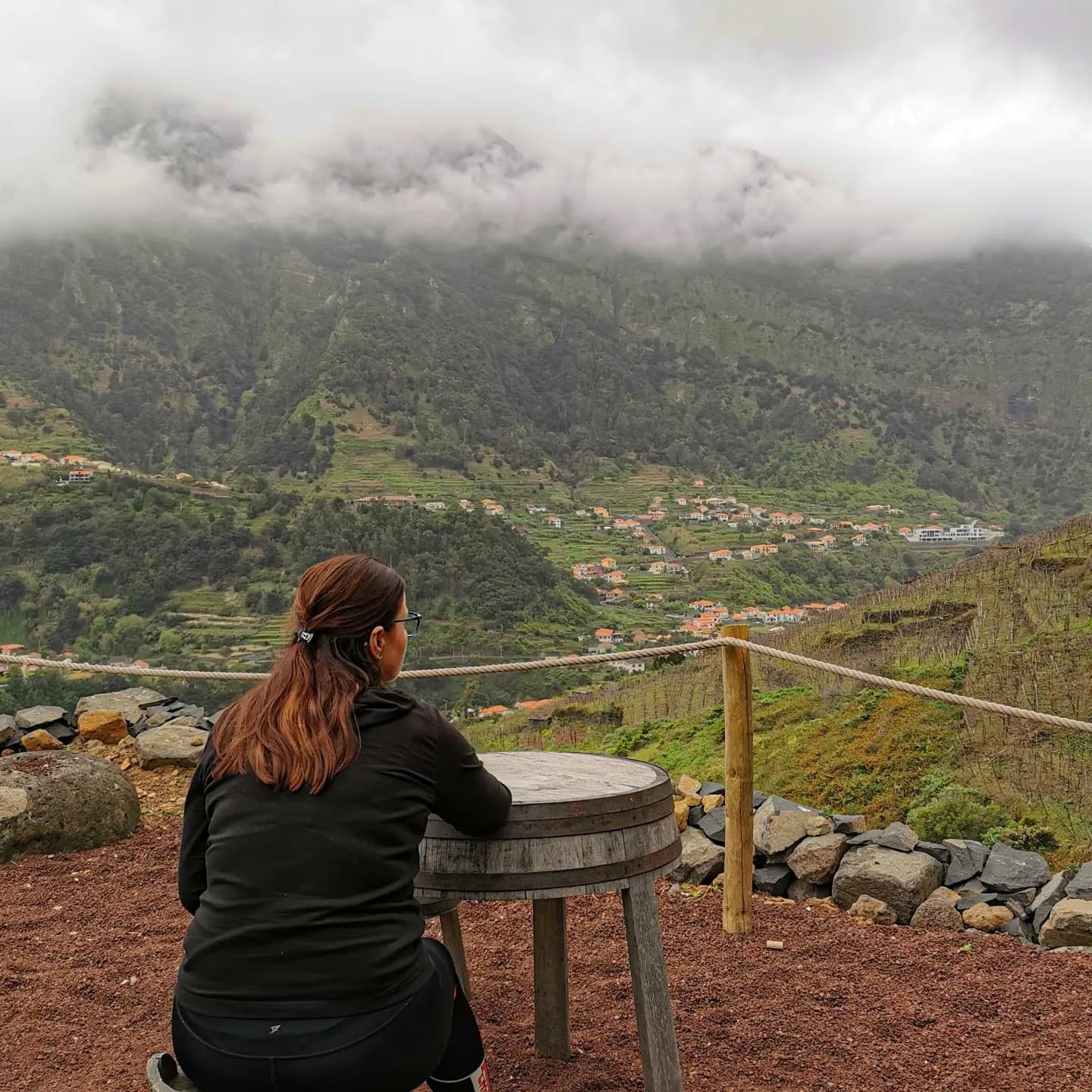 Person seated at viewpoint overlooking terraced valley and clouds
