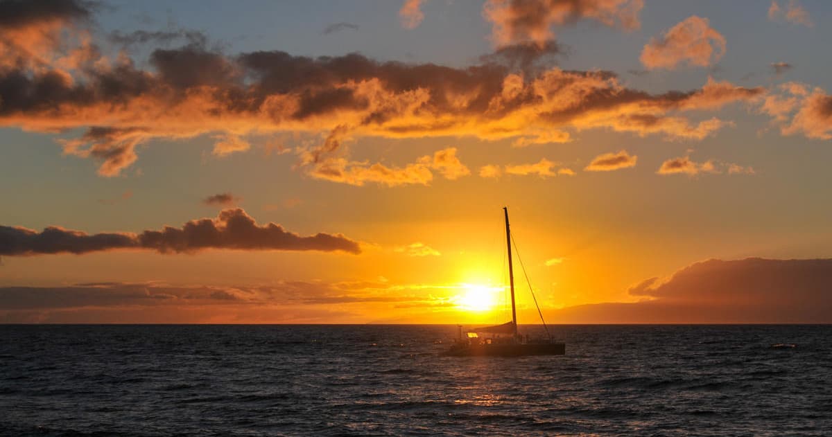 Sailboat silhouette cruising at sea during golden sunset