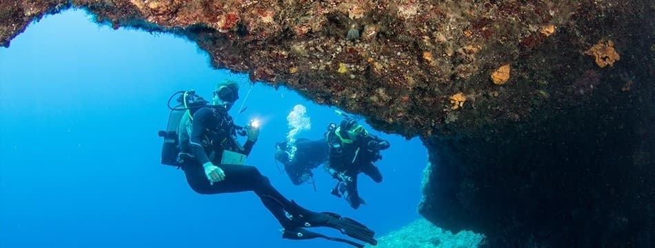 Scuba divers exploring dramatic underwater cave and reef