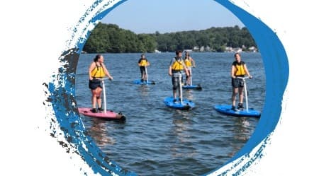 Stand-up paddleboarders paddling on calm lake near treed shoreline