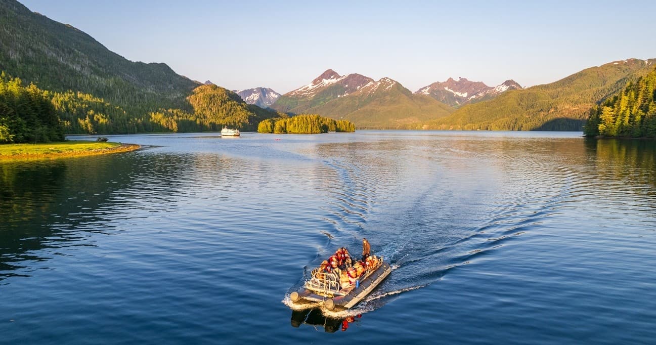 Small zodiac cruising lake with mountain vistas at sunset Alaska