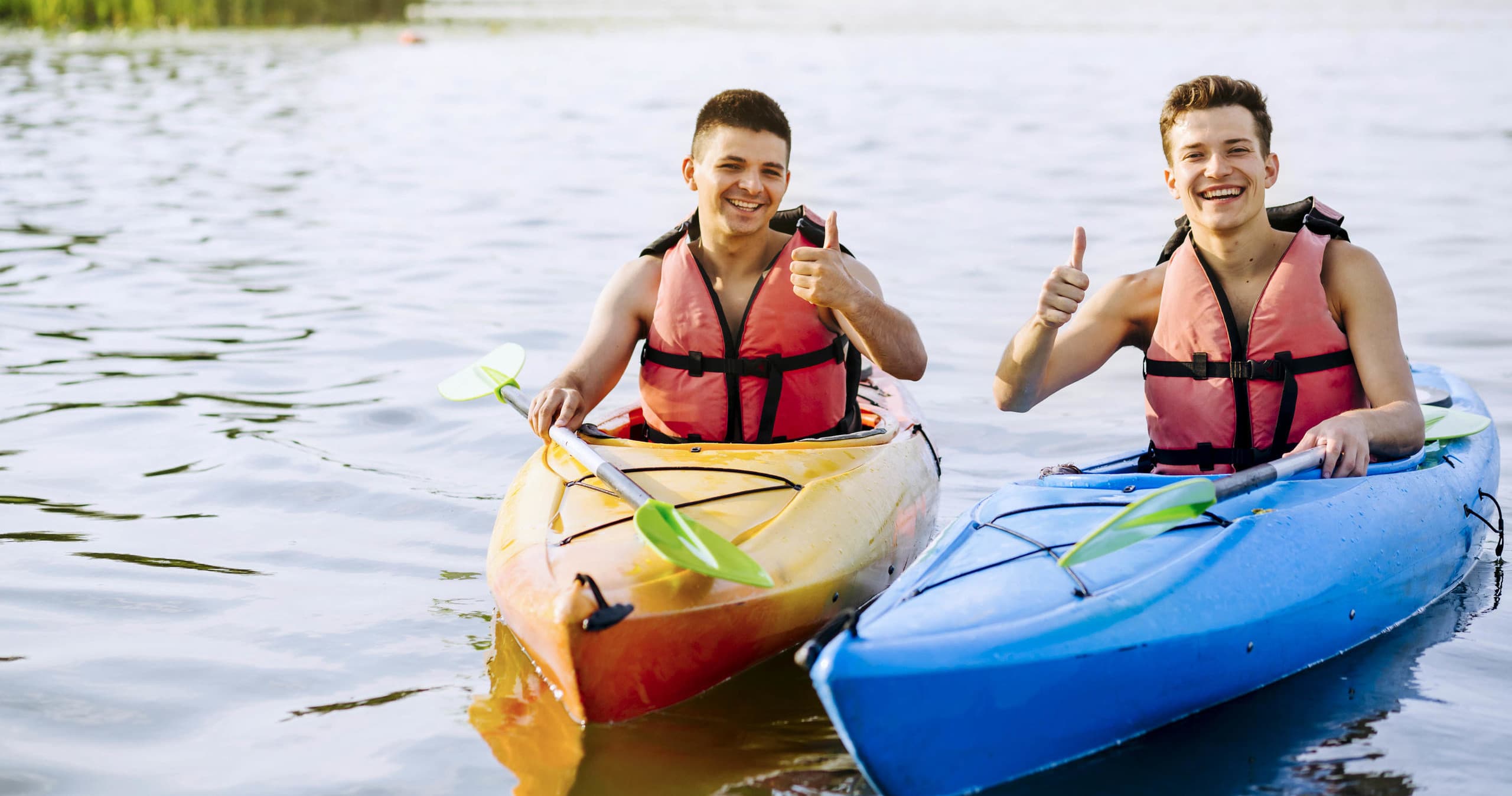 Two kayakers paddling on calm lake shore, recreational kayaking