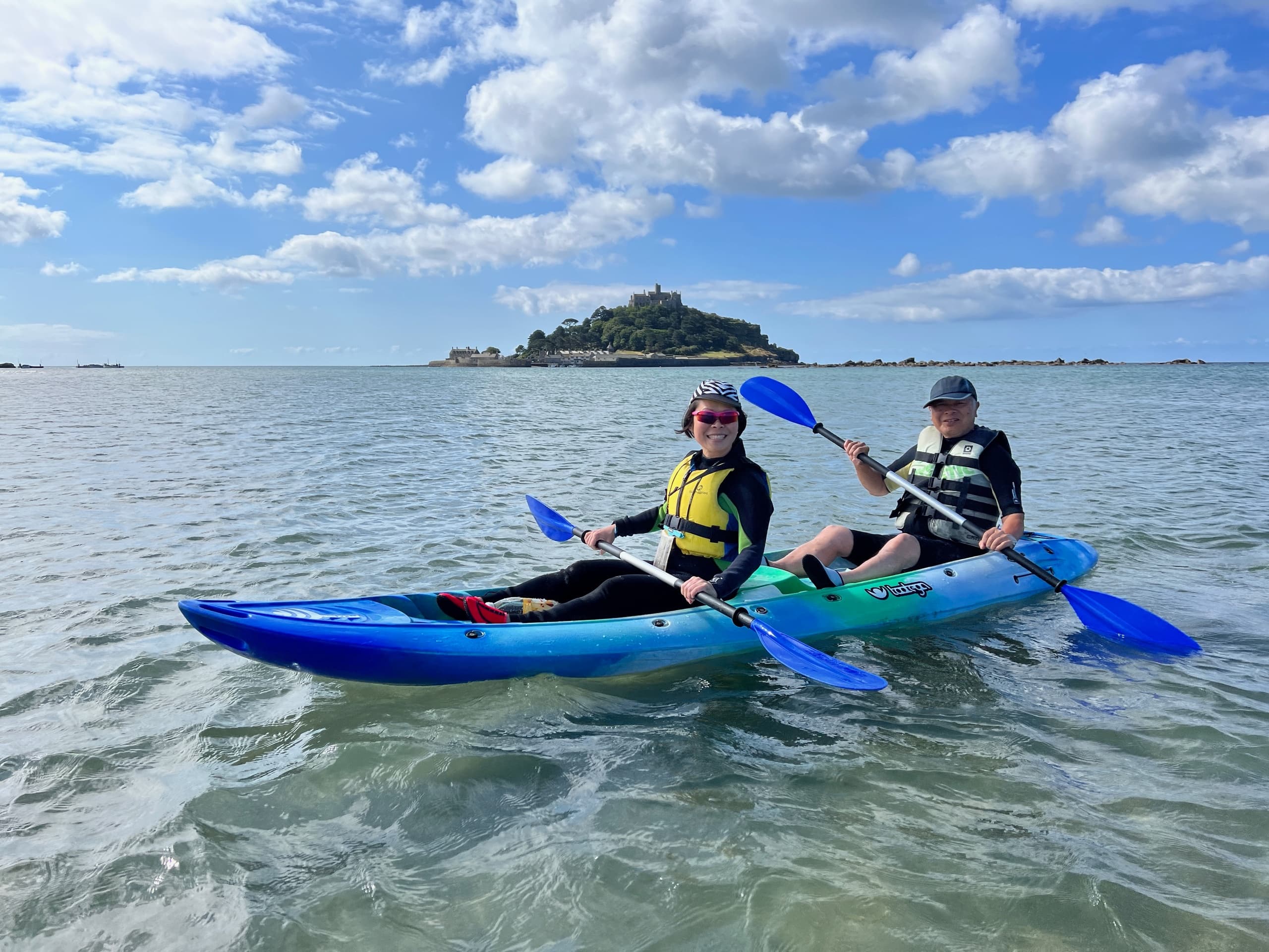 Two kayakers paddling near island on calm coastal waters