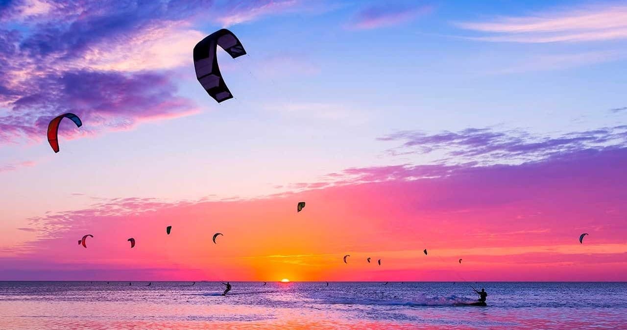Kitesurfers silhouetted against colorful sunset over ocean