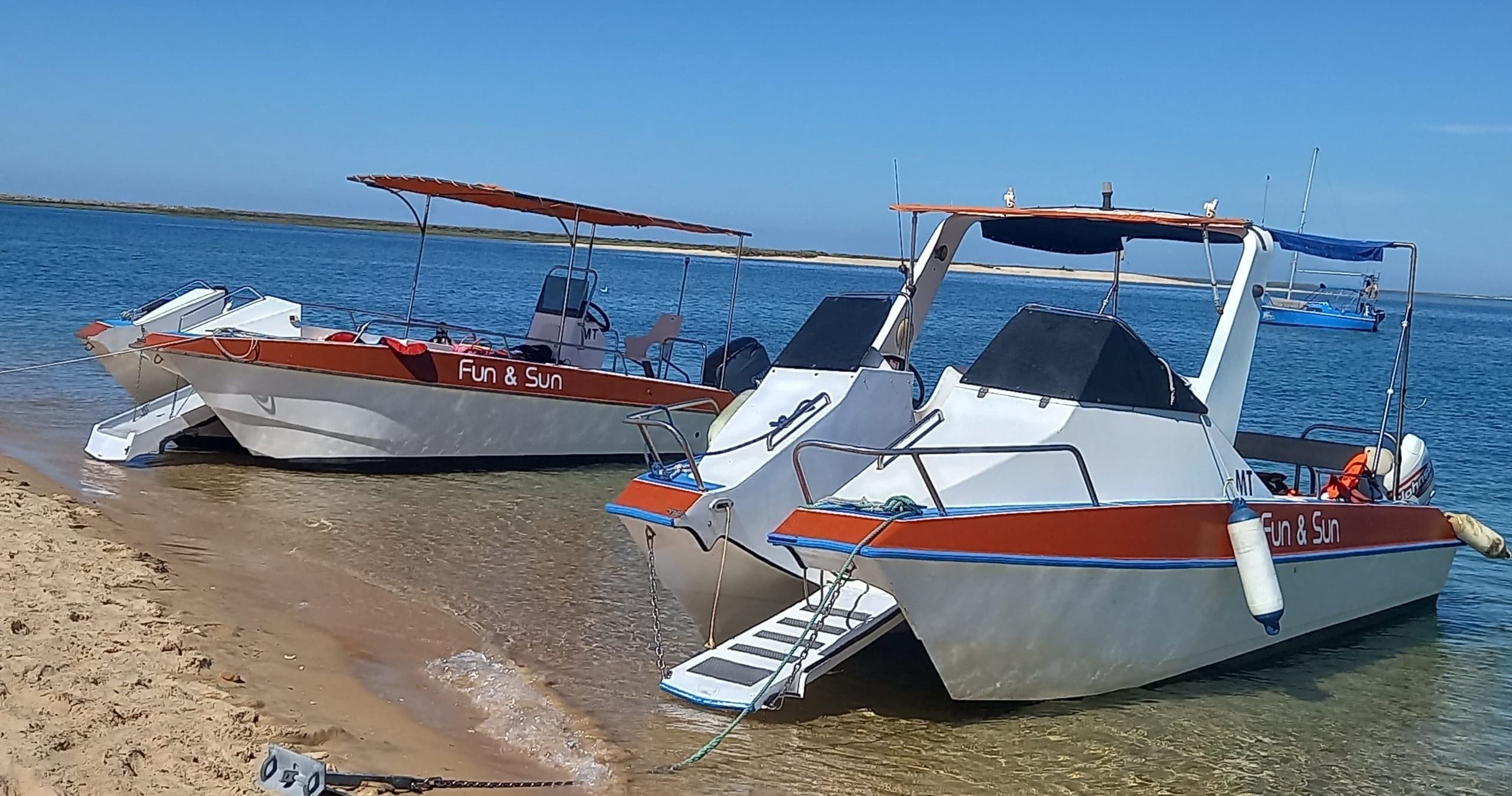 Twin excursion boats beached on sandy shoreline under blue sky